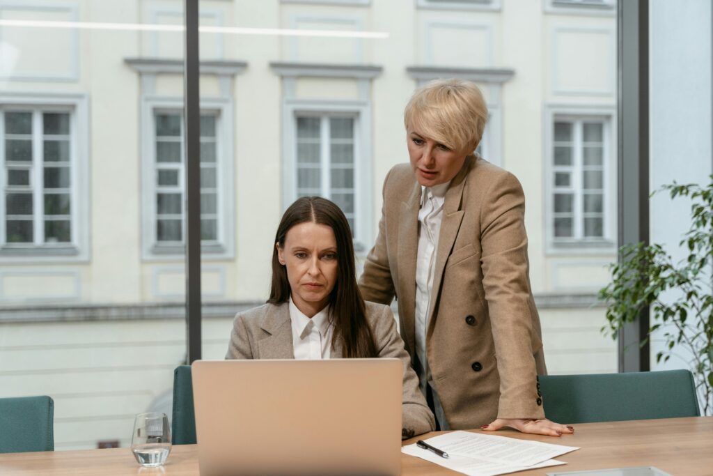 Two businesswomen in an office setting collaborating with a laptop and documents.